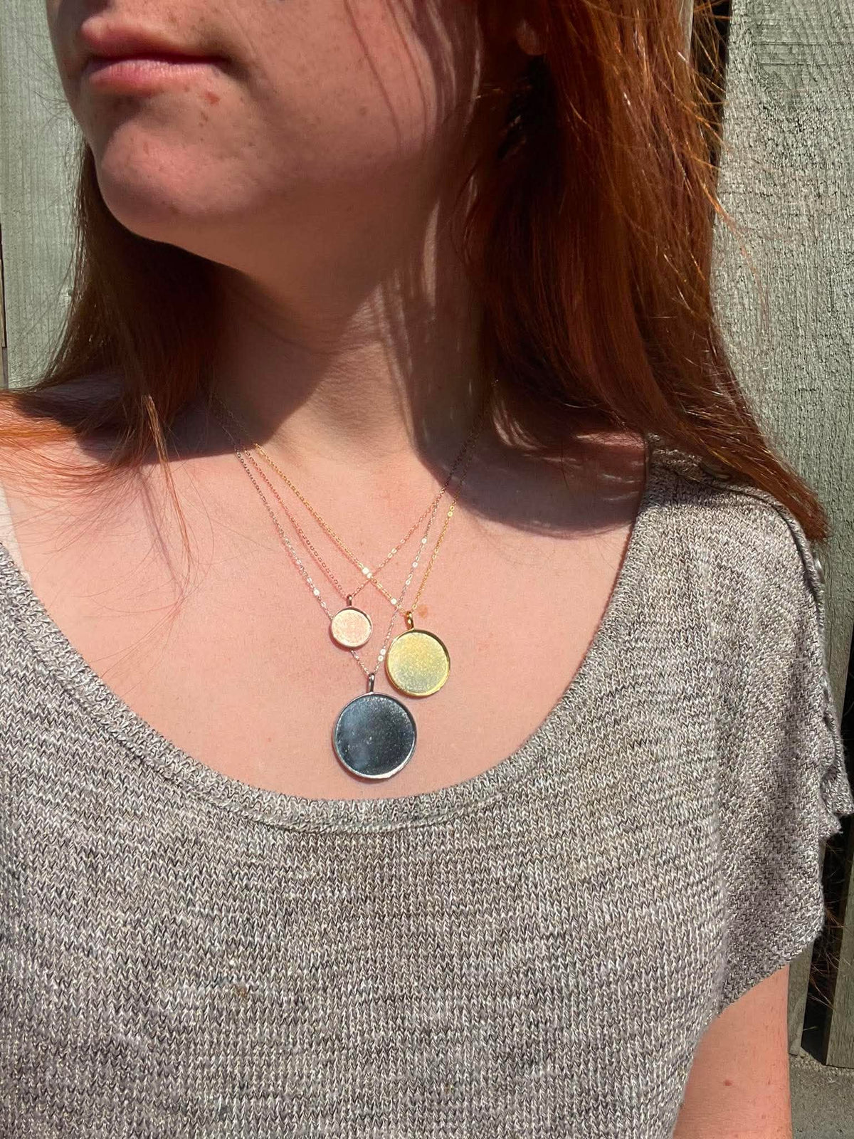 3 circle pendants in 3 different sizes displayed on a women wearing them. Meant to be filled with ashes or breastmilk.