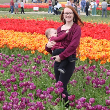 a mother breastfeeding her baby while standing in a tulip field.