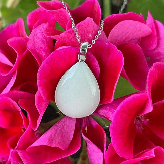 Silver teardrop-shaped breastmilk keepsake necklace displayed against vibrant pink flowers.