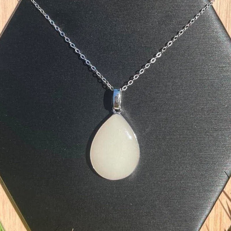 Silver teardrop-shaped breastmilk keepsake necklace with a soft white stone, displayed on a black backdrop.