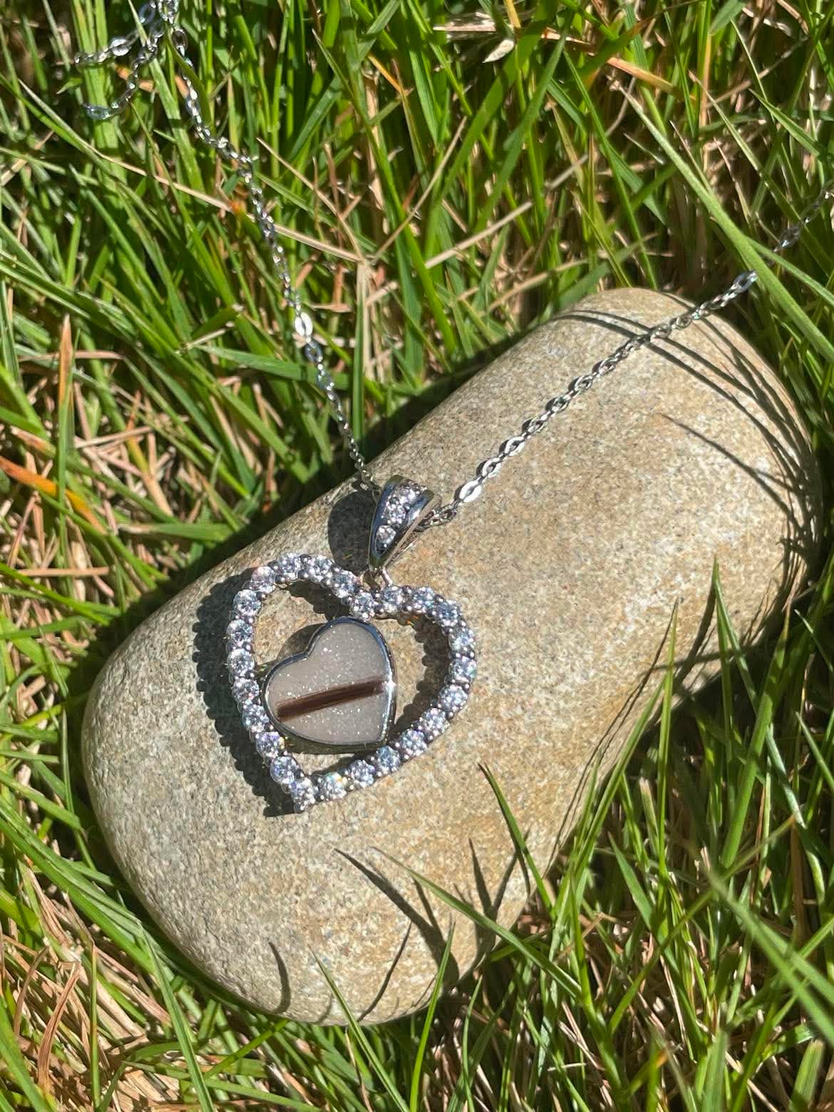 Heart necklace filled with breastmilk and baby strands of hair, displayed on a rock in sunlight.