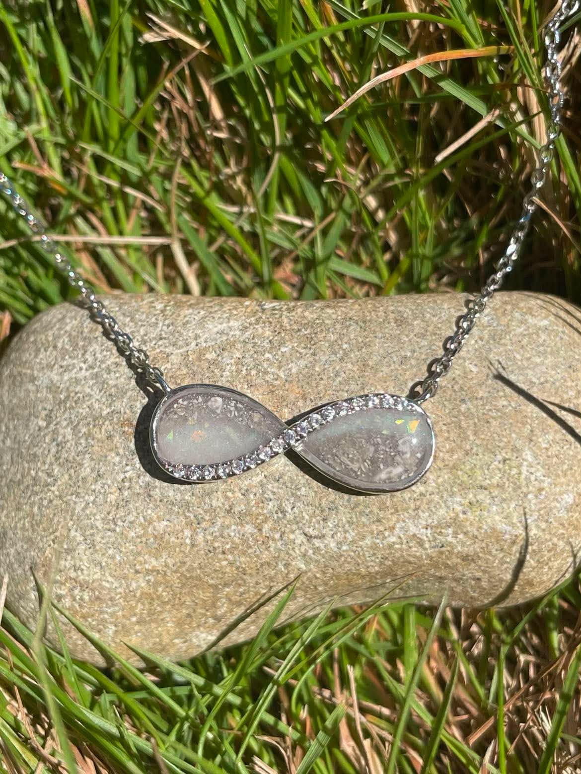 Silver Infinity necklace filled with ashes and breastmilk displayed on a rock in the sunlight.