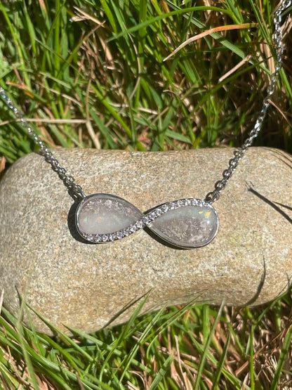 Silver Infinity necklace filled with ashes and breastmilk displayed on a rock in the sunlight.