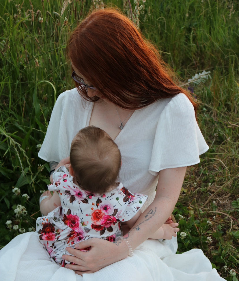 a mother breastfeeding her baby while looking down at the child lovingly and wearing a keepsake necklace.