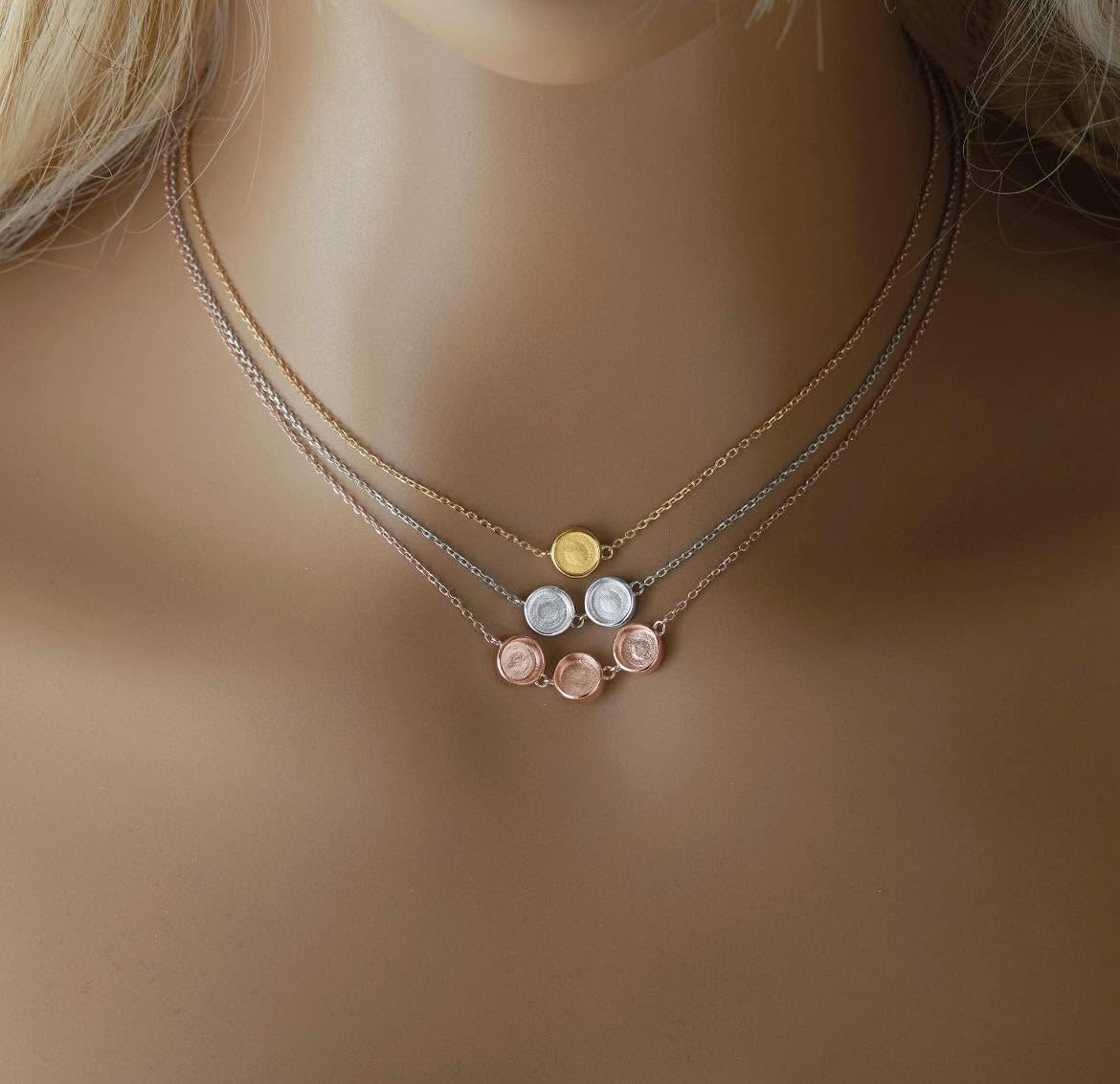 A close-up of a model's neck wearing a layered necklace set. The set features three delicate chains in gold, silver, and rose gold, with small round disc charms at the center and larger rose gold rose-shaped charms below.