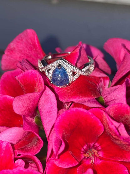 Silver teardrop-shaped pregnancy test keepsake ring with a blue center and sparkling crystal accents, displayed on bright pink flowers.